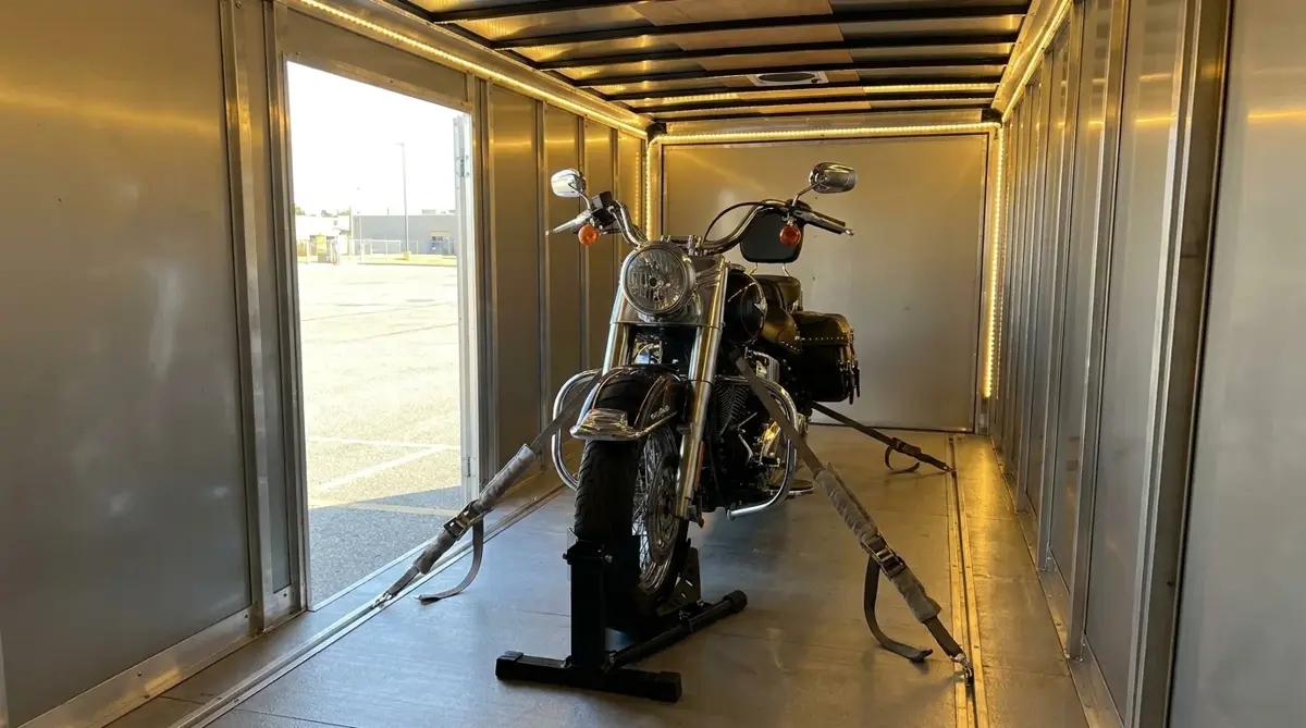 A cruiser motorcycle strapped upright in a wheel chock inside an enclosed trailer